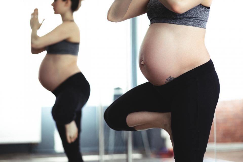 Spor kıyafetli hamile bir kadın, ayna karşısında tek ayak üzerinde denge duruşu yaparak egzersiz yapıyor